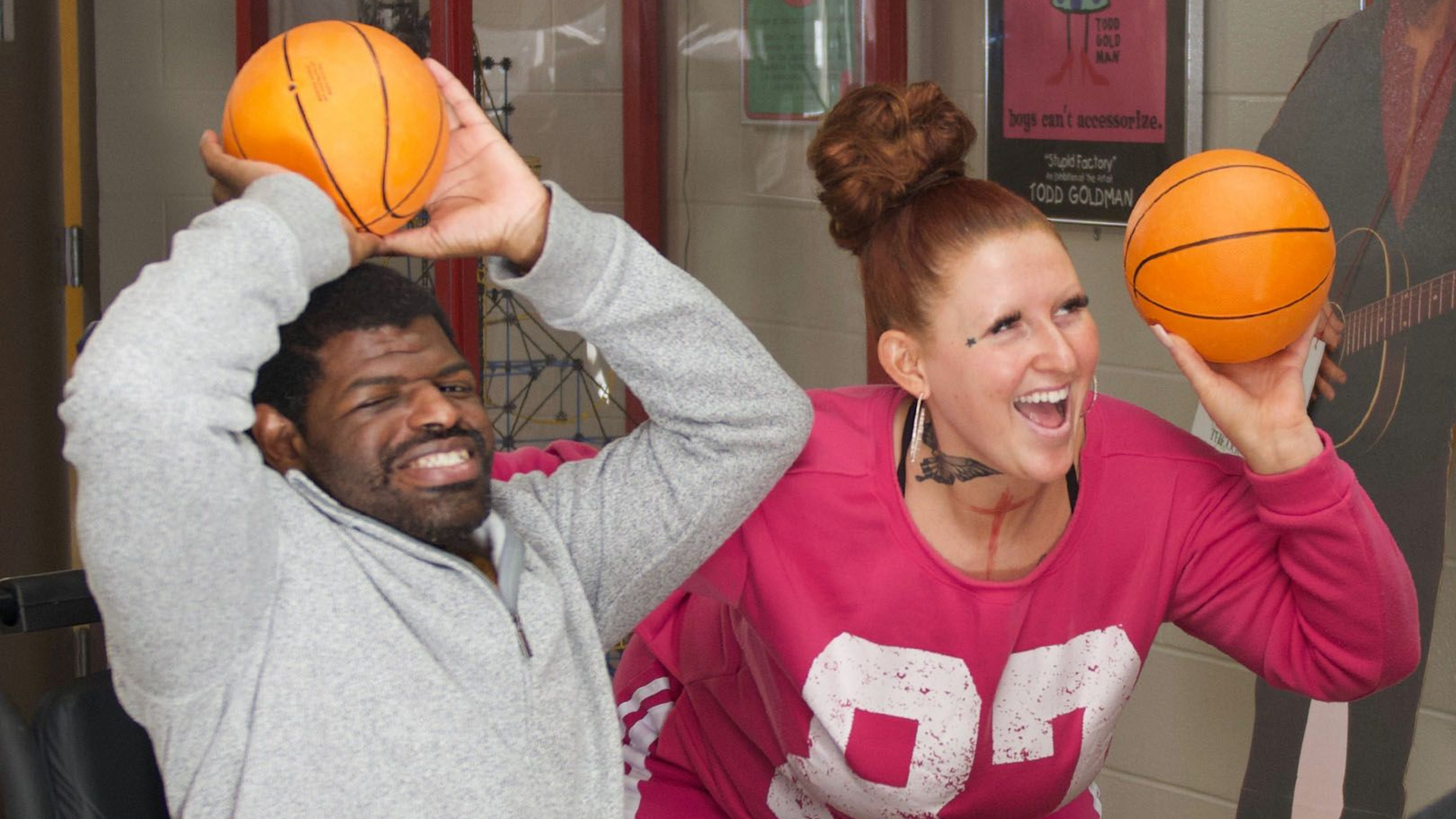 A man served by Orange Grove smiling alongside a staff member as they both throw mini basketballs.