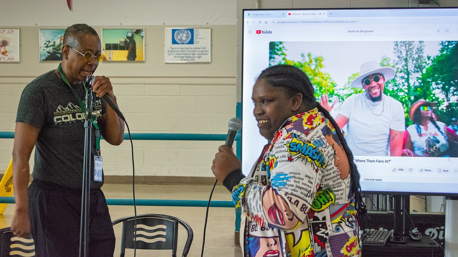 A female individual served by Orange Grove grins while holding a mircrophone during karaoke.