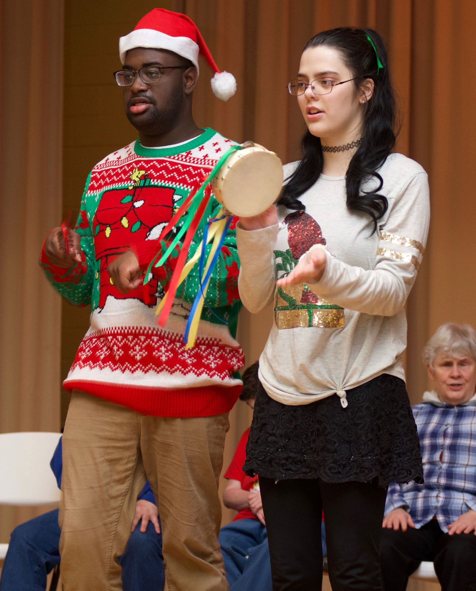 A young man and woman in Christmas attire sing and play a tambourine as part of a Orange Grove Music concert.