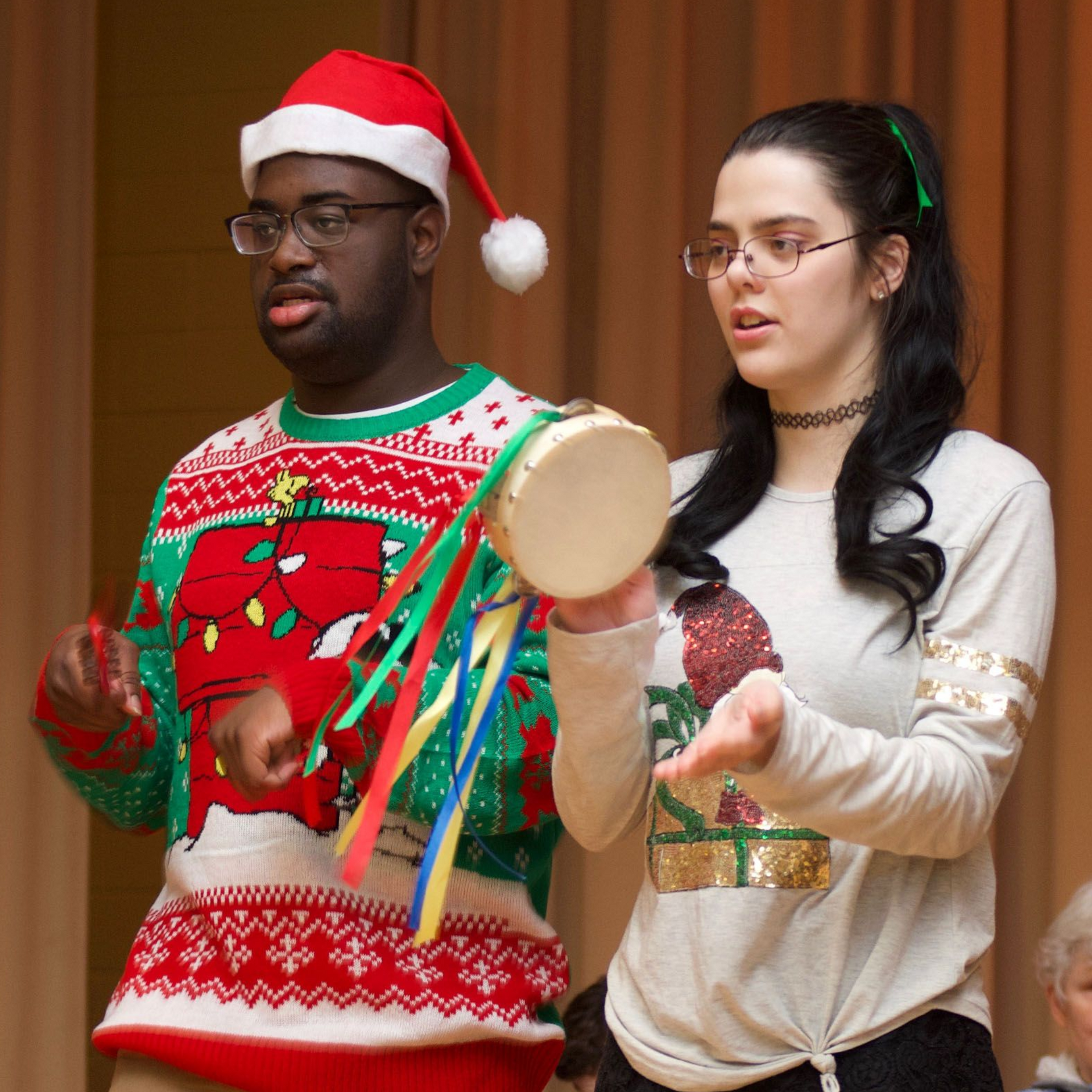 A young man and woman in Christmas attire sing and play a tambourine as part of a Orange Grove Music concert.