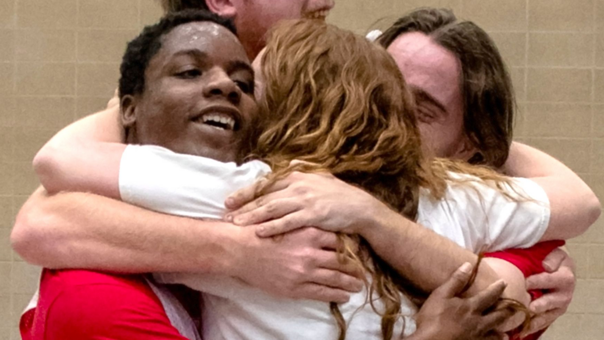 A group of four individuals served by Orange Grove in a group hug during a Special Olympics basketball game.