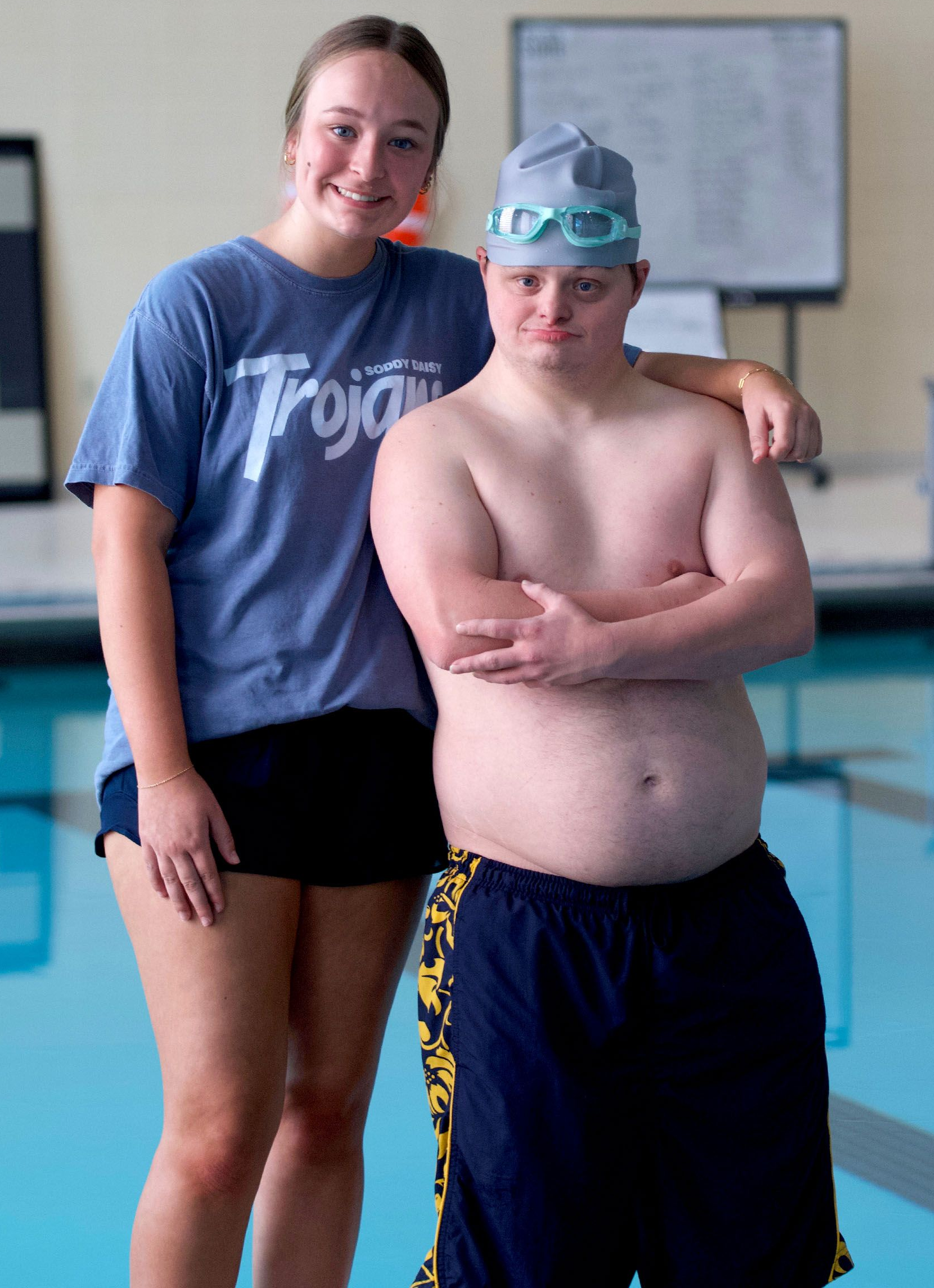 A male Special Olympics swimmer poses with his arms crossed, leaning on a smiling female staff member.