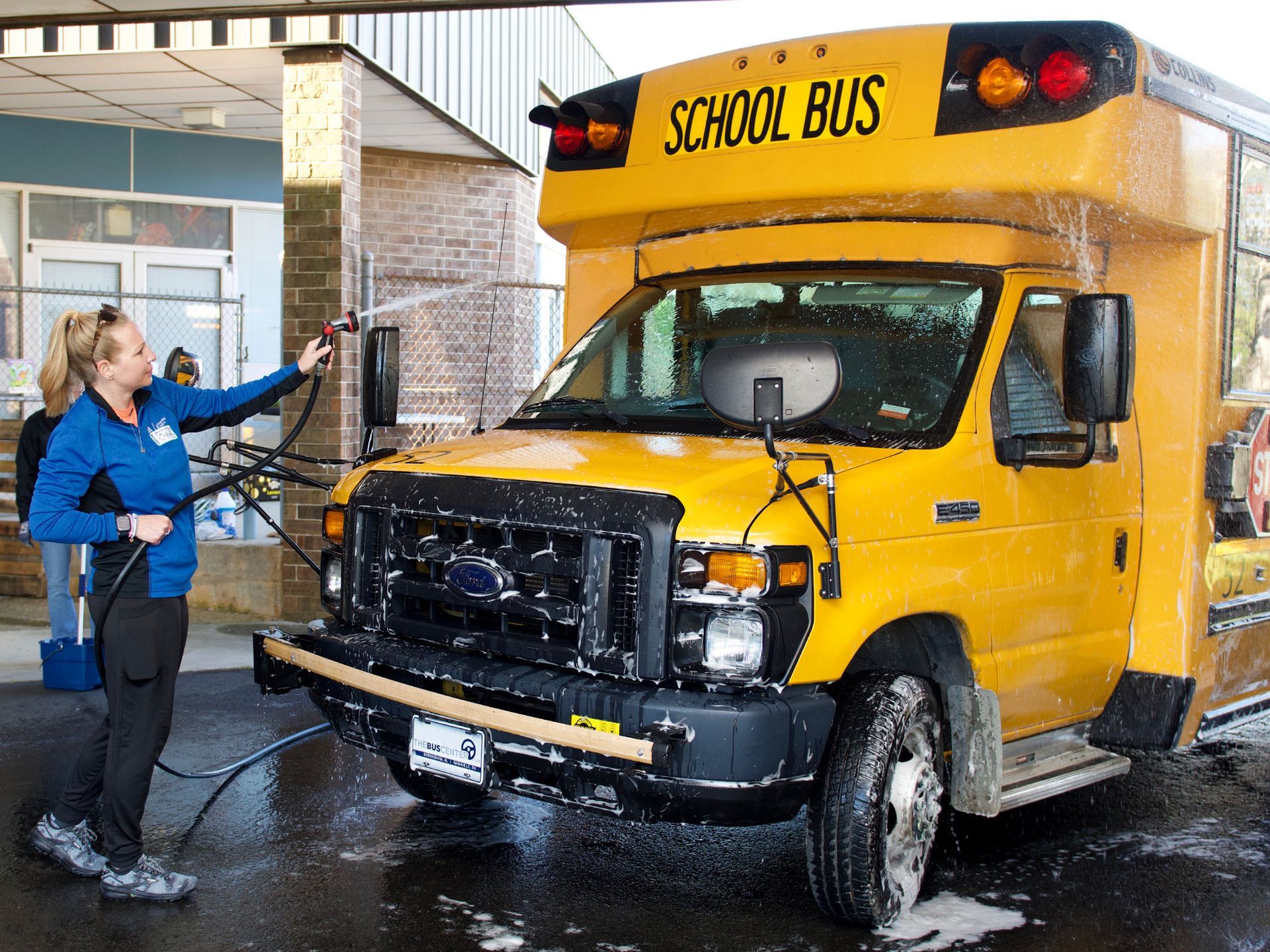 A female volunteer washing off a yellow Orange Grove Center school bus.