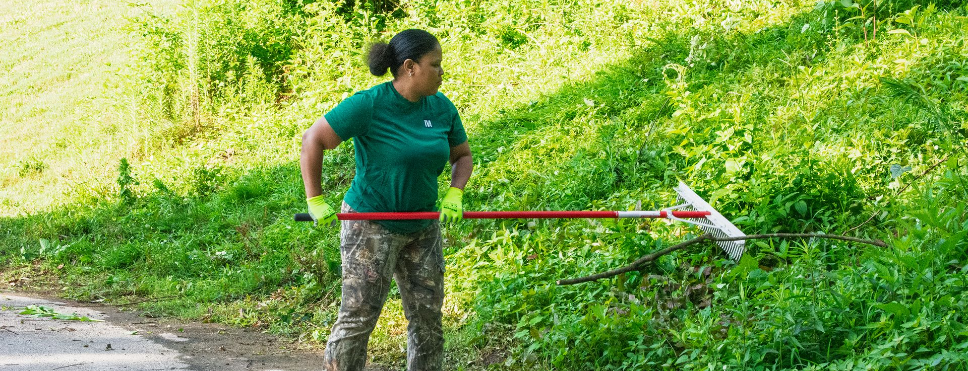 A female TVA volunteer raking overgrown weeds during a landscaping project at a residential home.