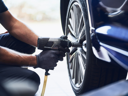 Mechanic tightening a car wheel lug nut with a pneumatic impact wrench