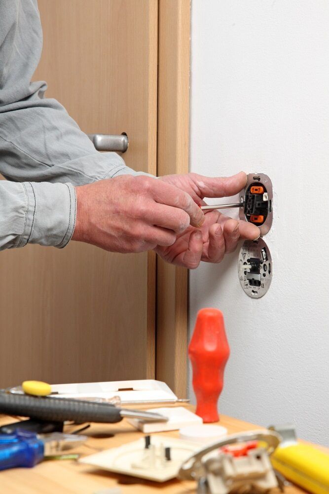 A Man Is Fixing A Light Switch On A Wall — J.A.F. Electrical Solutions in Kawana, QLD