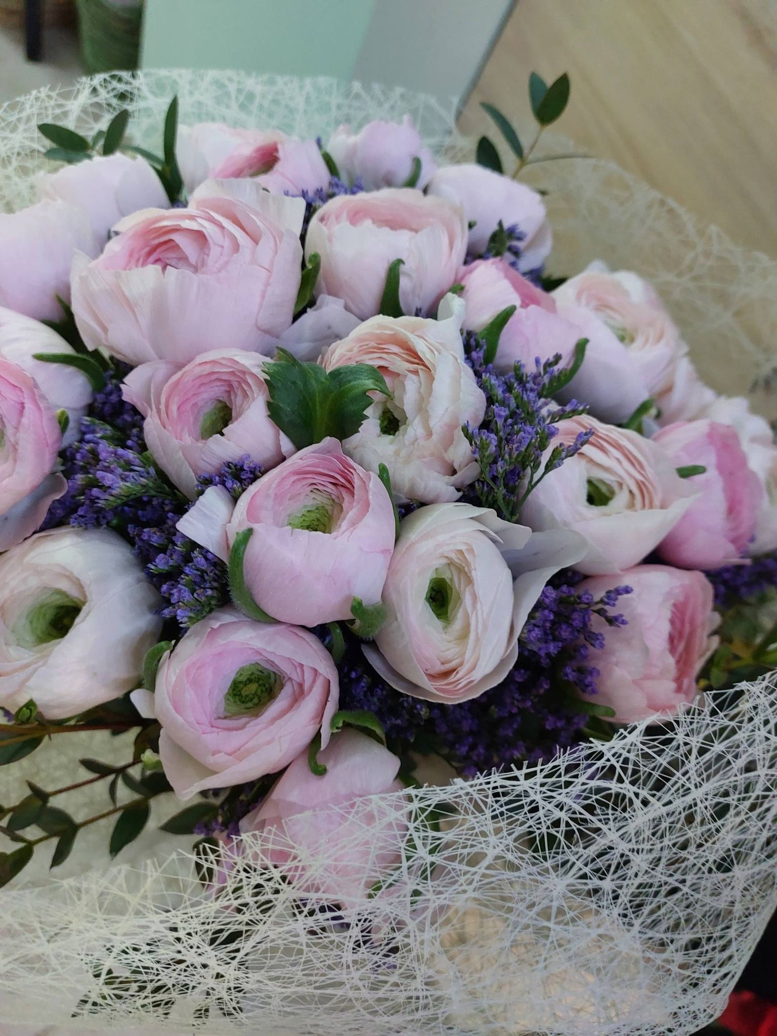 Bouquet di ranuncoli rosa chiaro e fiori viola, avvolti in una rete.