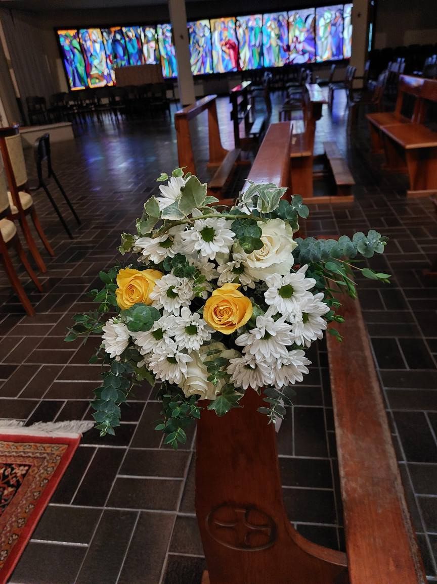 Composizione floreale con rose gialle e margherite bianche su una panca della chiesa. Vetrata colorata sullo sfondo.