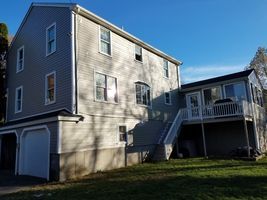Two-story beige house with garage, exterior stairs, and a small deck in daylight