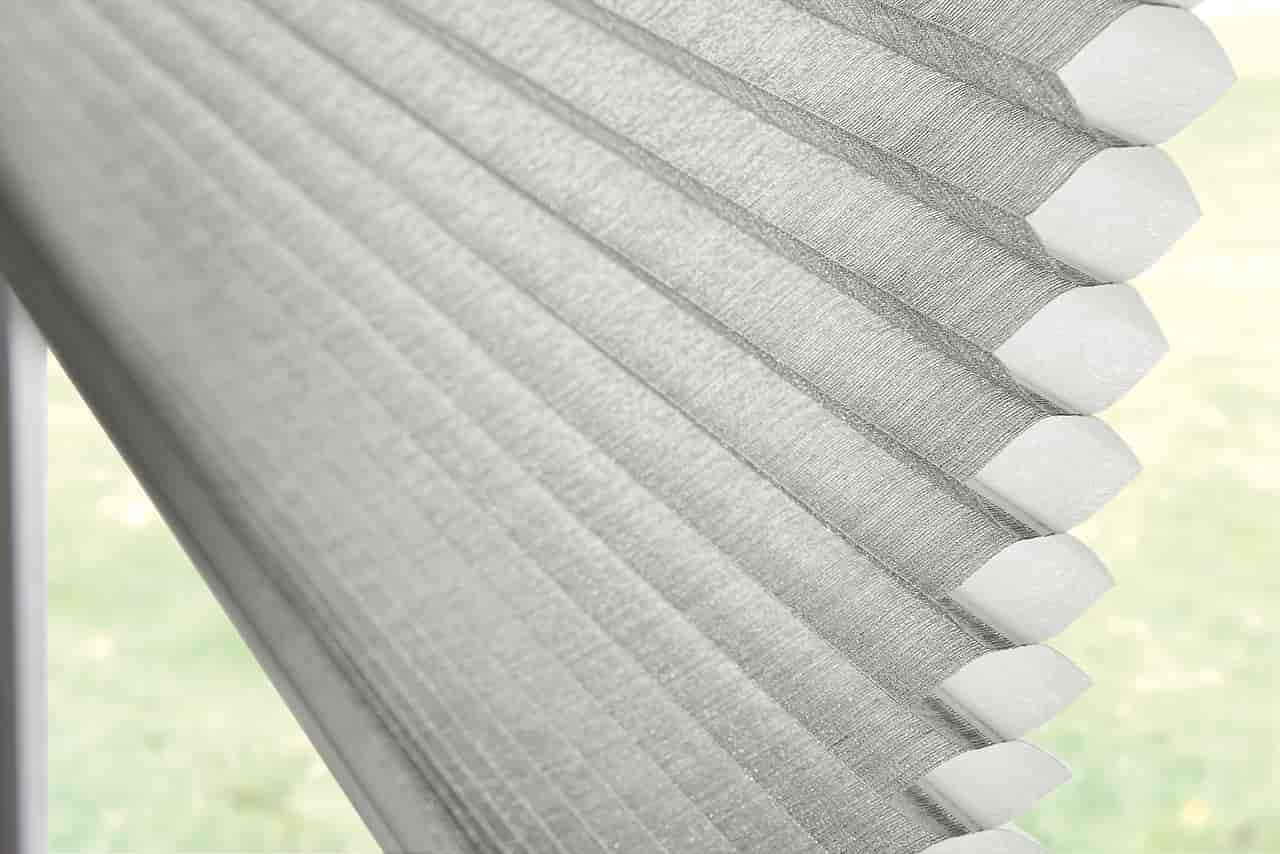 Close-up of white pleated window blinds with scalloped edges against a bright window.