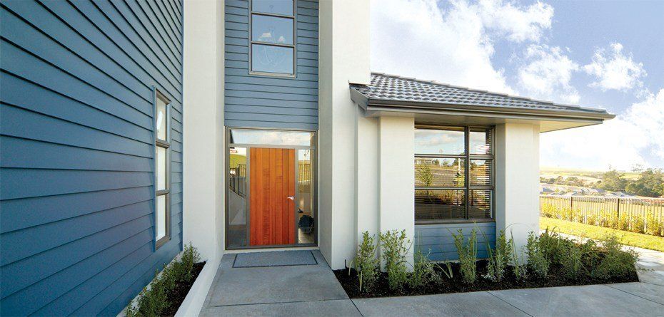 Modern house exterior with blue siding, orange door, and large windows. James Hardie Sidings | MasterCraft Roofing, Siding & Windows | Serving Eastern MA, NH & Selected Areas of VT