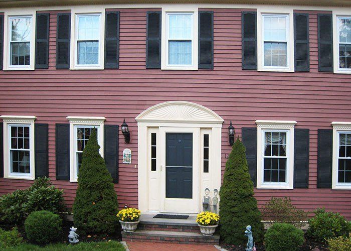 Red house with white-trimmed windows and black shutters. Front door framed by a white arch. Energy Efficient | MasterCraft Roofing, Siding & Windows | Serving Eastern MA, NH & Selected Areas of VT
