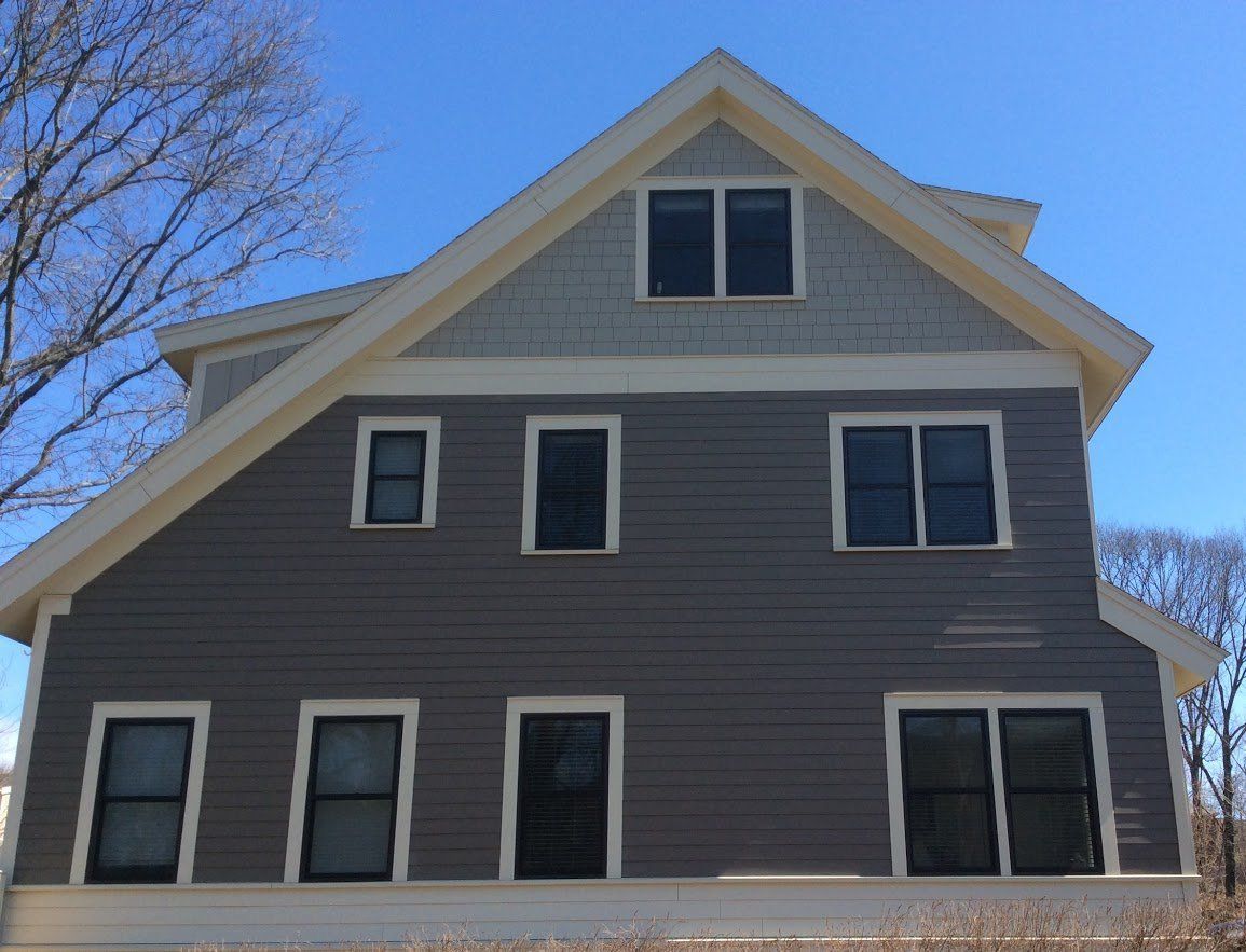 Gray house with white trim and multiple windows against a blue sky