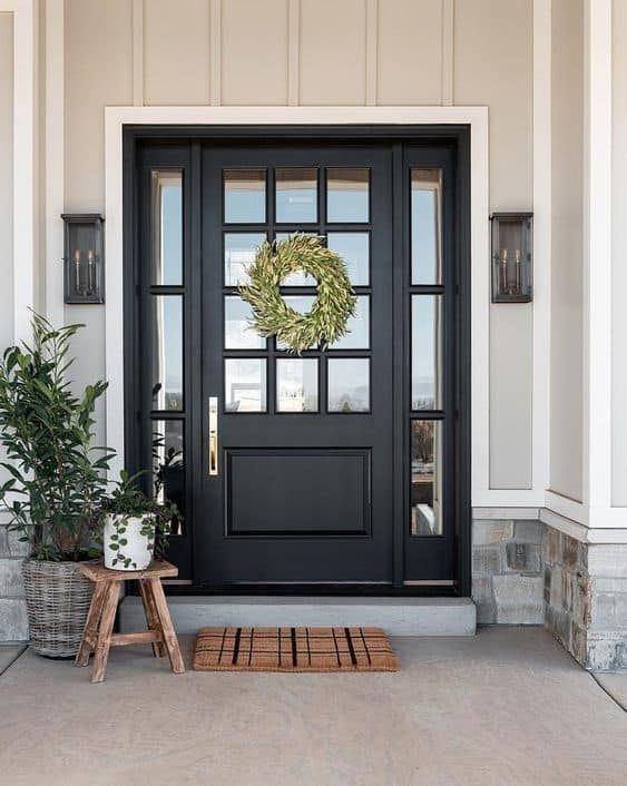 Front porch with a dark blue front door, green wreath, potted plants, and a striped welcome mat.