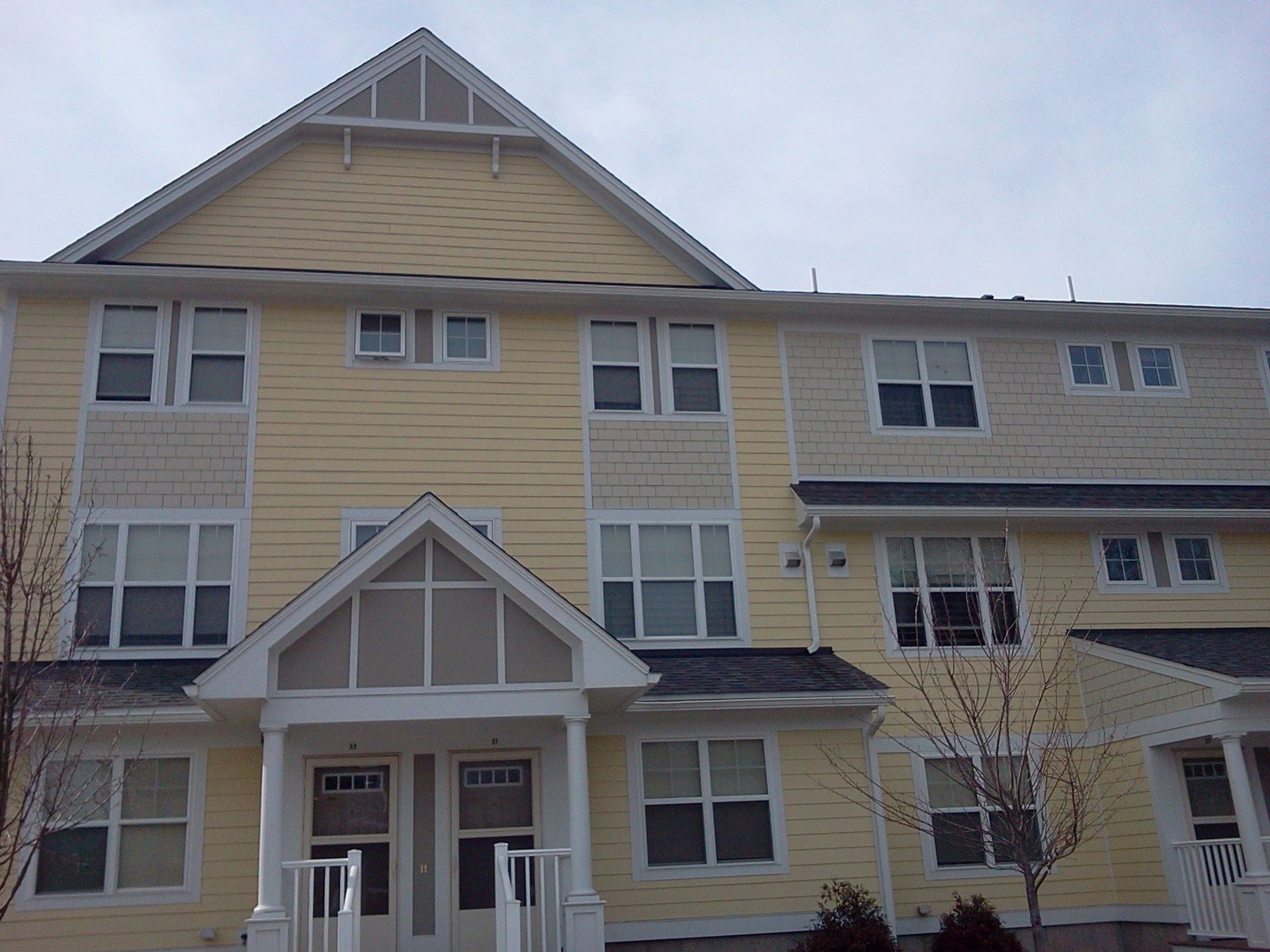 Yellow apartment building with white trim and a covered front entrance under an overcast sky