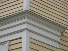 Close-up of a house corner with white decorative trim under beige siding.