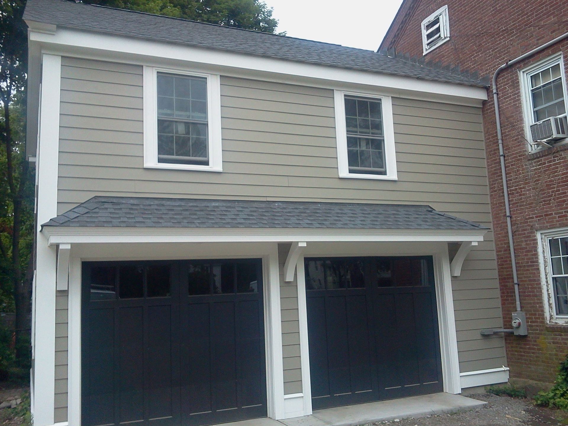 Two-story tan house with a white trim and double black garage doors under a gabled roof.