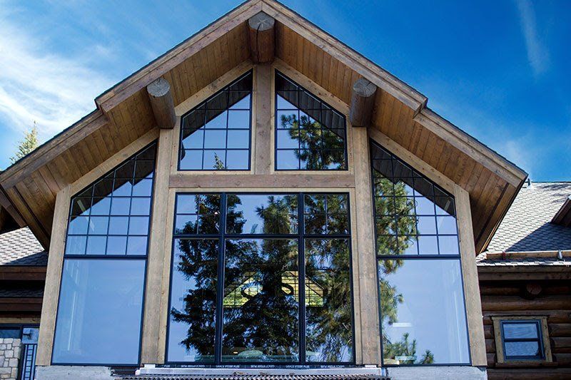 Front view of a wooden cabin with large triangular windows and a blue sky reflection