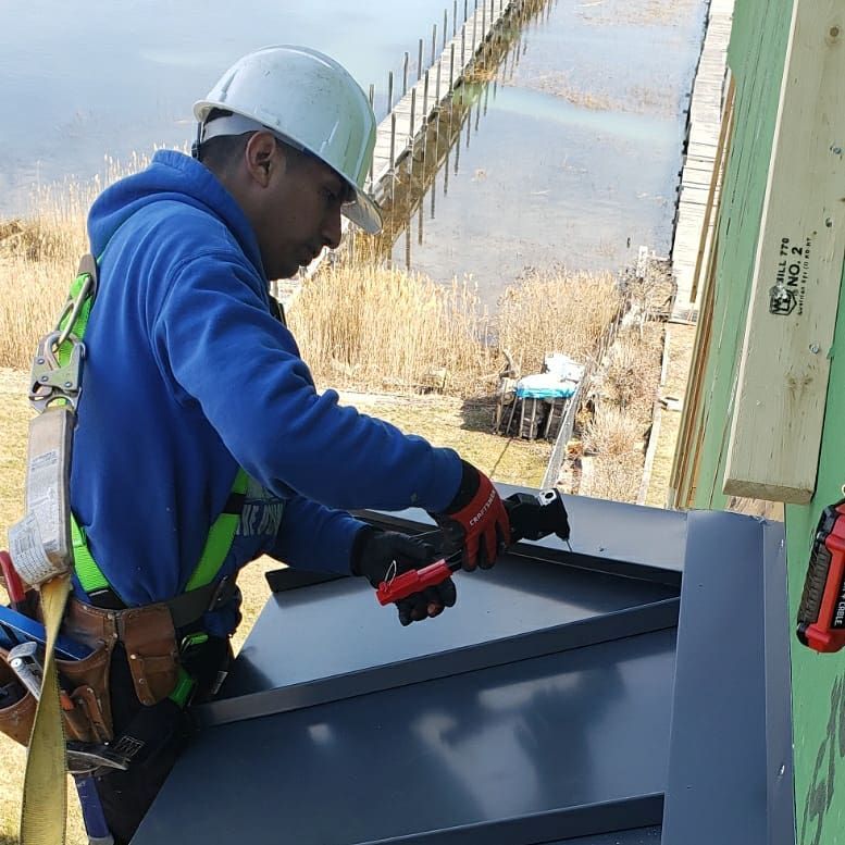 Worker in hard hat installing a metal panel outdoors beside a sloped water channel