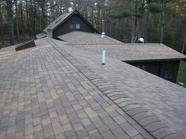 Wide gray shingled roof with a dormer and surrounding trees in the background