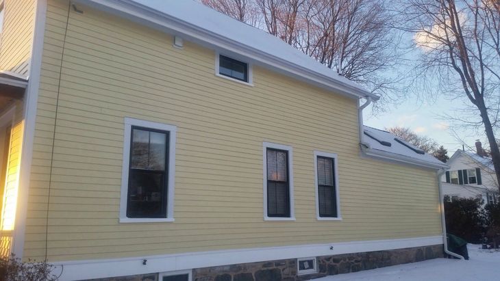 Yellow house exterior with white trim and snow on the roof in a winter neighborhood.