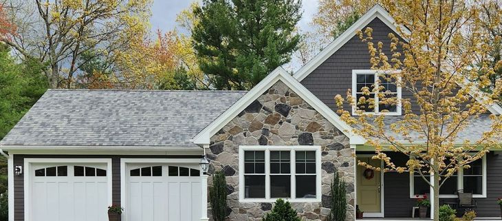 Suburban house with stone facade, white garage doors, and autumn trees in front