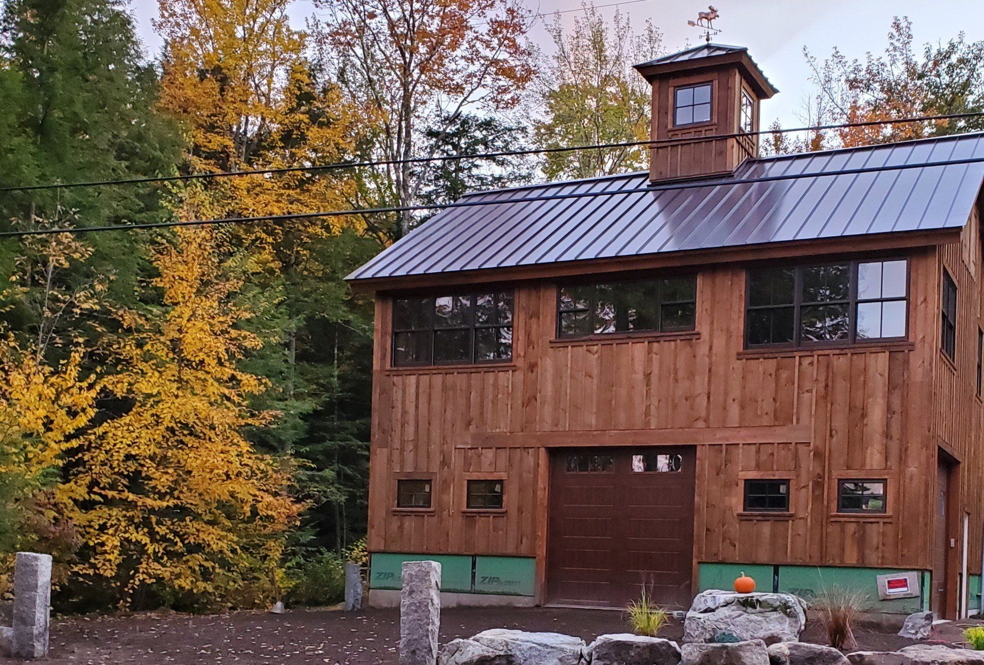 Wooden barn-style building with a metal roof, surrounded by autumn trees and rocks