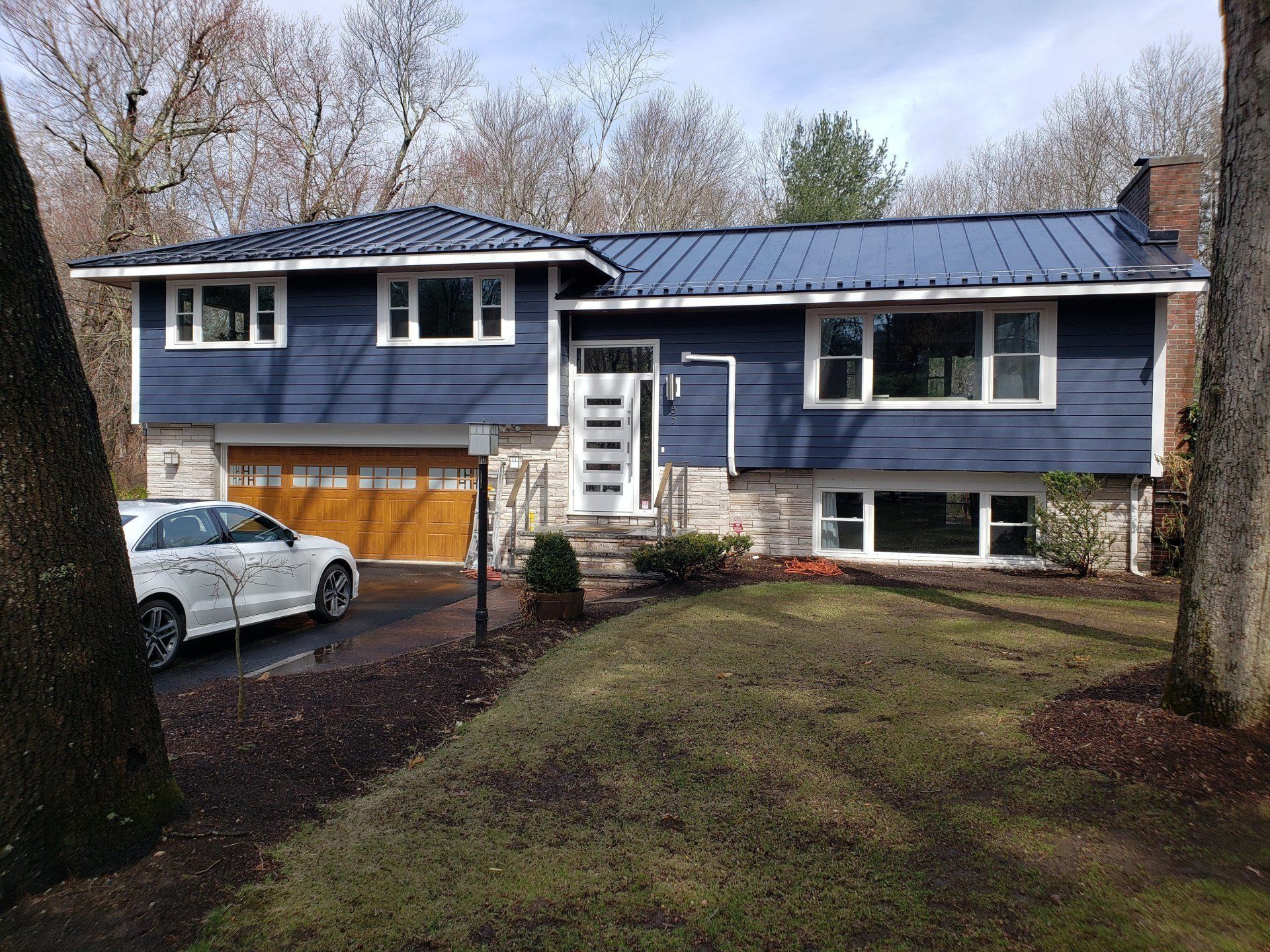 Blue suburban house with solar panels, white garage, and parked car on a sloped front yard