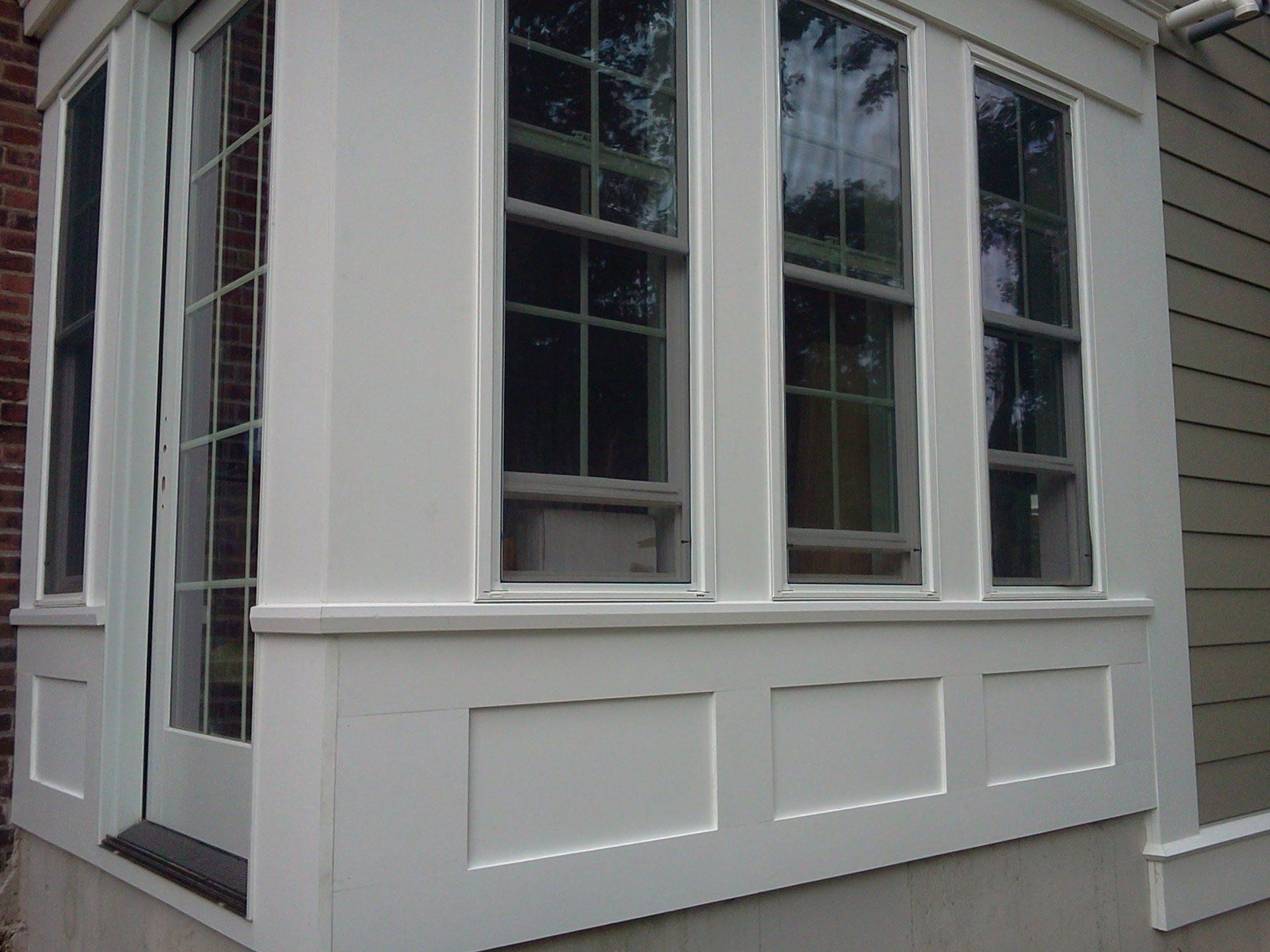 White bay window on gray house exterior with decorative panels beneath it