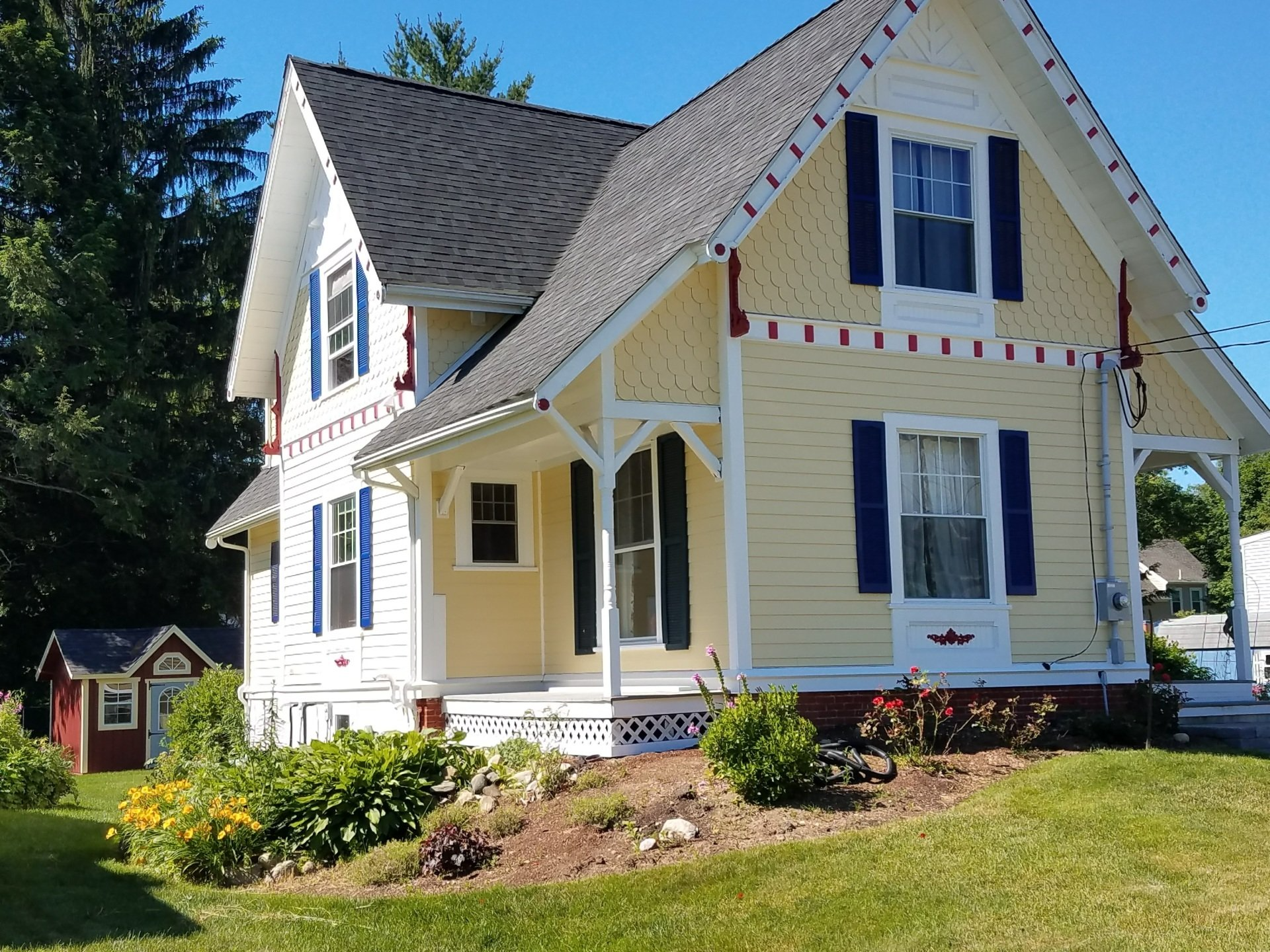 White house with blue shutters and trim, front porch, and flower garden on a sunny lawn