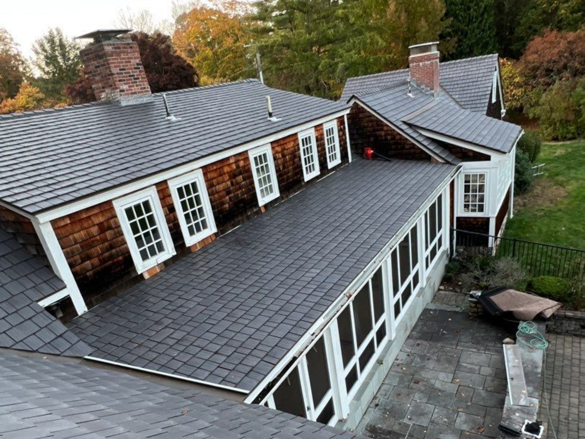 Aerial view of a house with a dark gray roof and multiple white-framed windows amid autumn trees