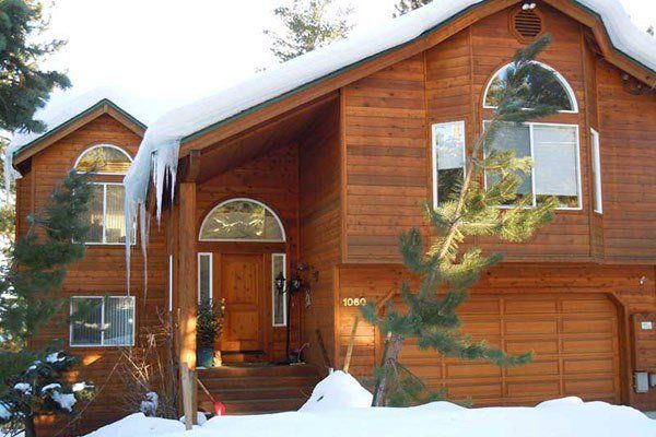 Two-story brown wood house with snow on the roof and icicles, with a covered entryway and garage. Ice Dams | MasterCraft Roofing, Siding & Windows | Serving Eastern MA, NH & Selected Areas of VT