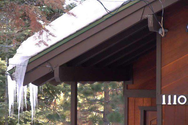 Icicles hanging from a brown roof with snow. The house number 1110 is visible. Roofing Repairs | MasterCraft Roofing, Siding & Windows | Serving Eastern MA, NH & Selected Areas of VT