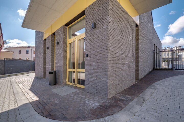 Modern building entrance with brick columns, yellow-framed glass doors, and paved walkway