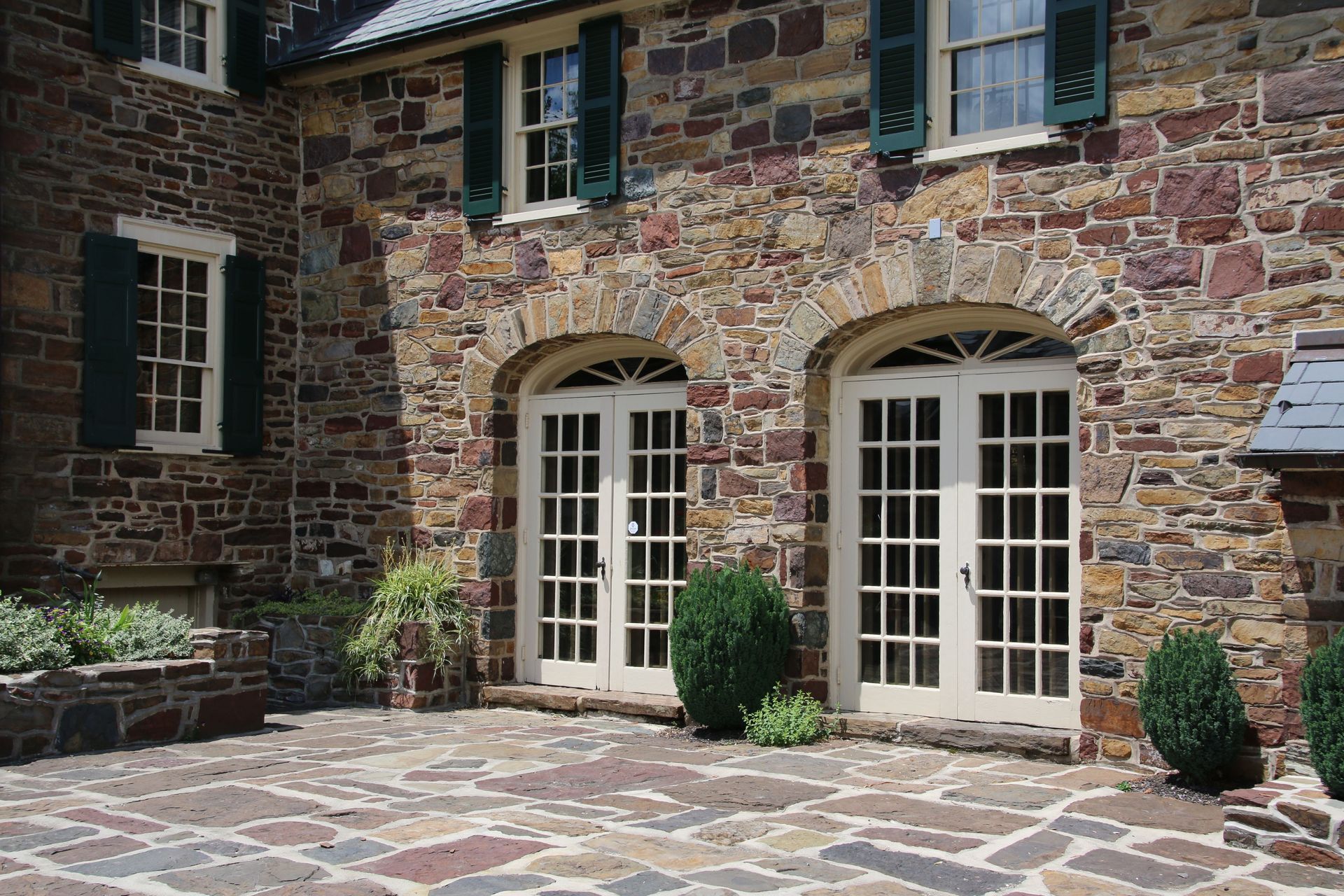 Stone courtyard with arched French doors and windows on a rustic building facade