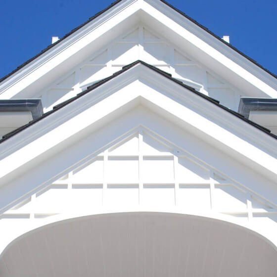 White gabled house roof with blue sky above and an arched front entrance below