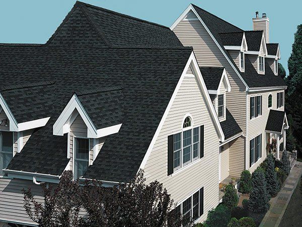Two-story house with black shingled roof, cream siding, and multiple dormers. Roofing | MasterCraft Roofing, Siding & Windows | Serving Eastern MA, NH & Selected Areas of VT