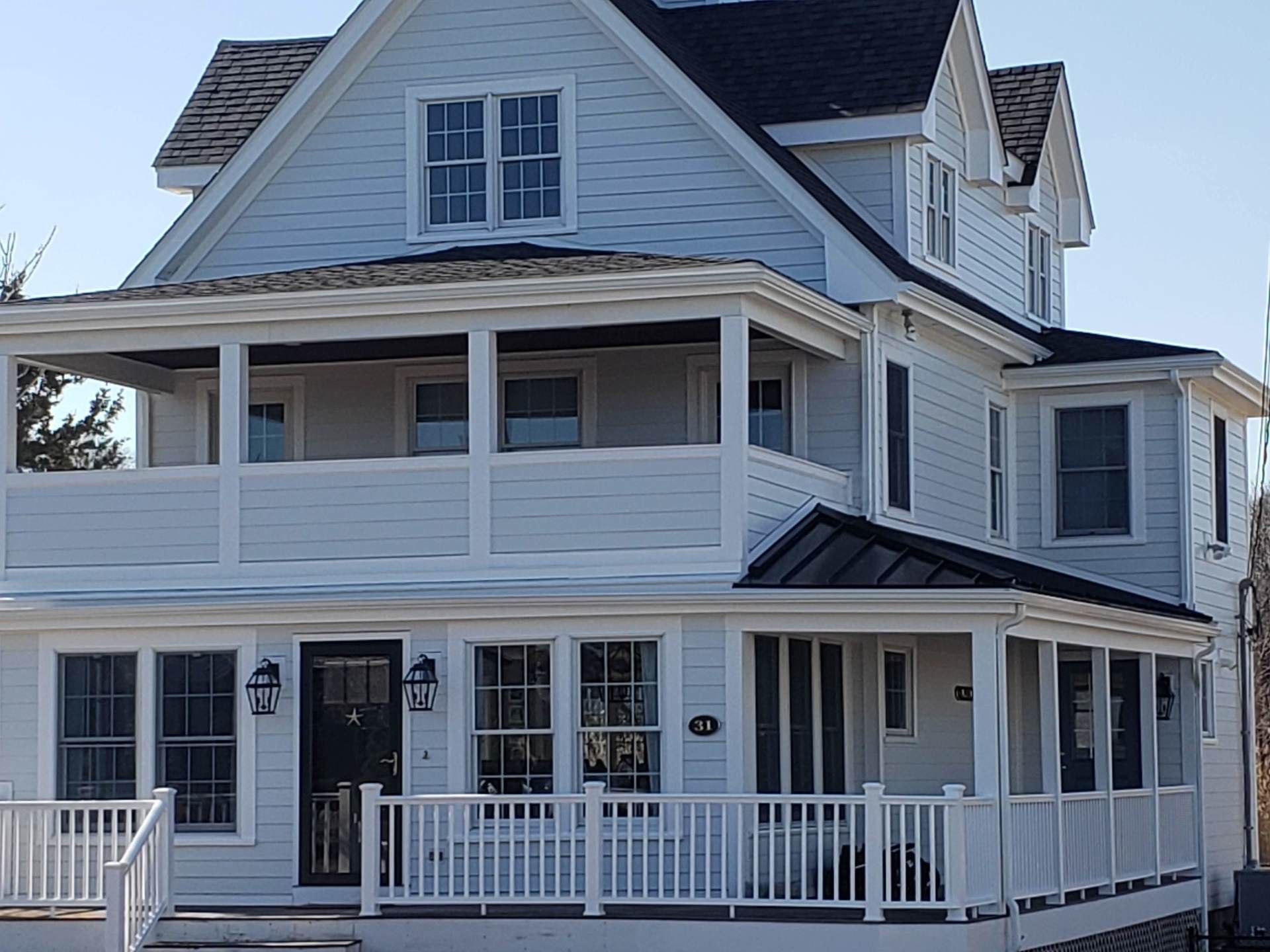 White two-story house with a wraparound porch and white railing under a dark roof