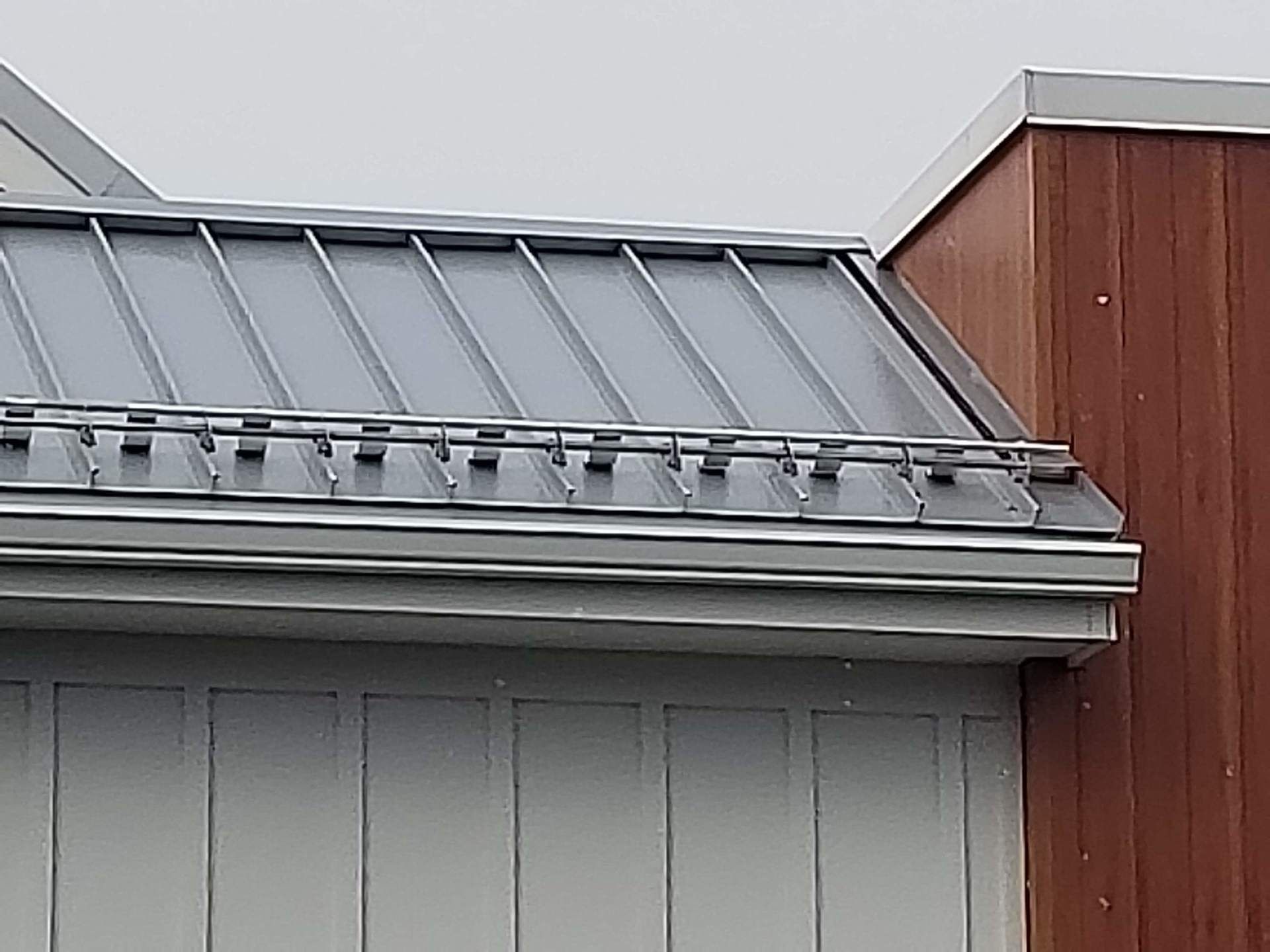Gray metal roof with skylights and a red-brown wall corner above a gray building facade