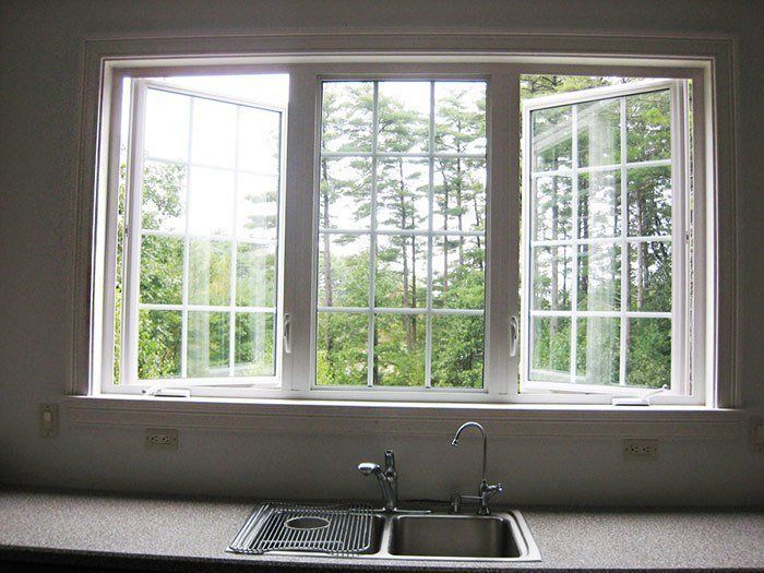 White-framed kitchen window with open casement windows, overlooking a forest. A sink sits below the window. Windows & Doors Gallery | MasterCraft Roofing, Siding & Windows | Serving Eastern MA, NH & Selected Areas of VT