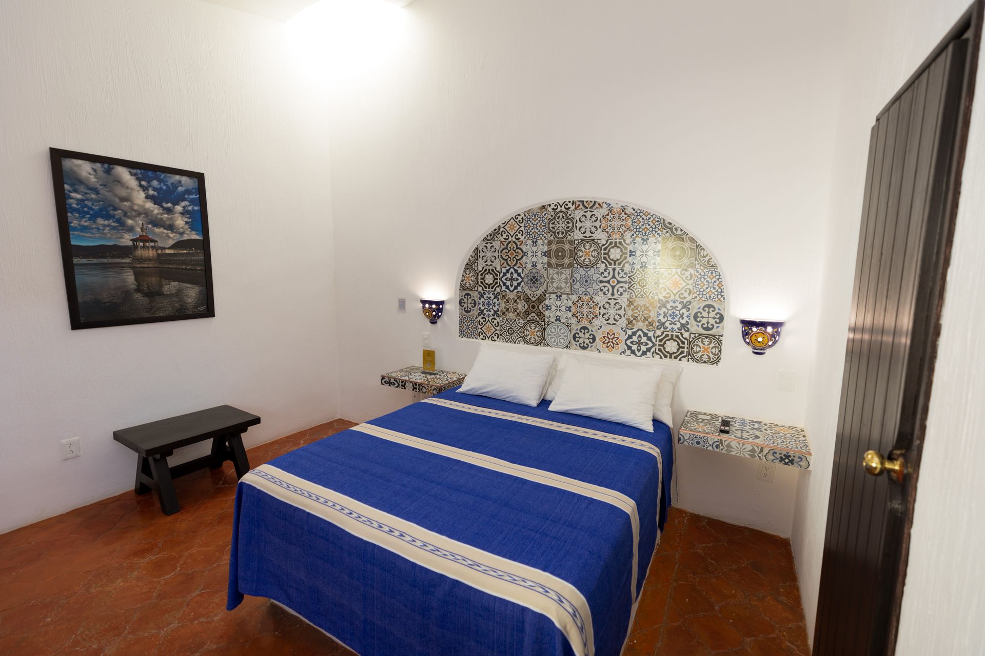 A bedroom with a blue bed and a picture on the wall.