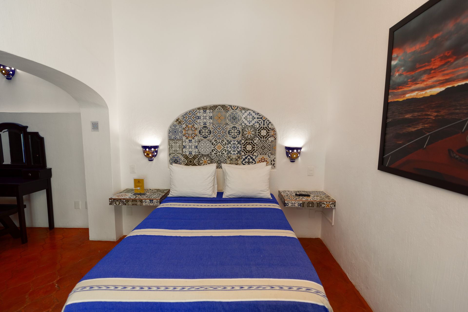 A bedroom with a blue bed and a painting on the wall
