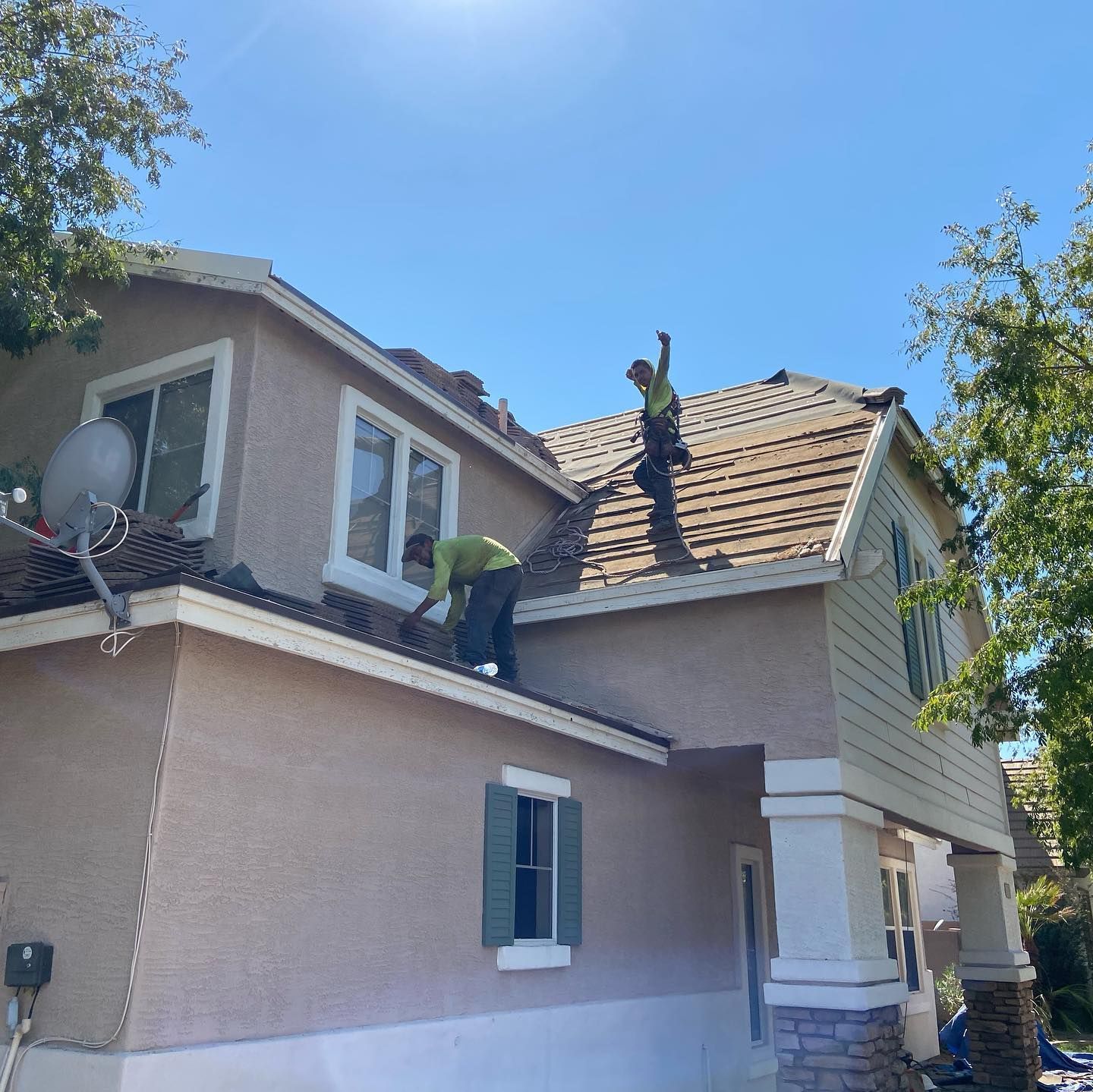 Three workers repairing a roof on a two-story house under a clear, blue sky.