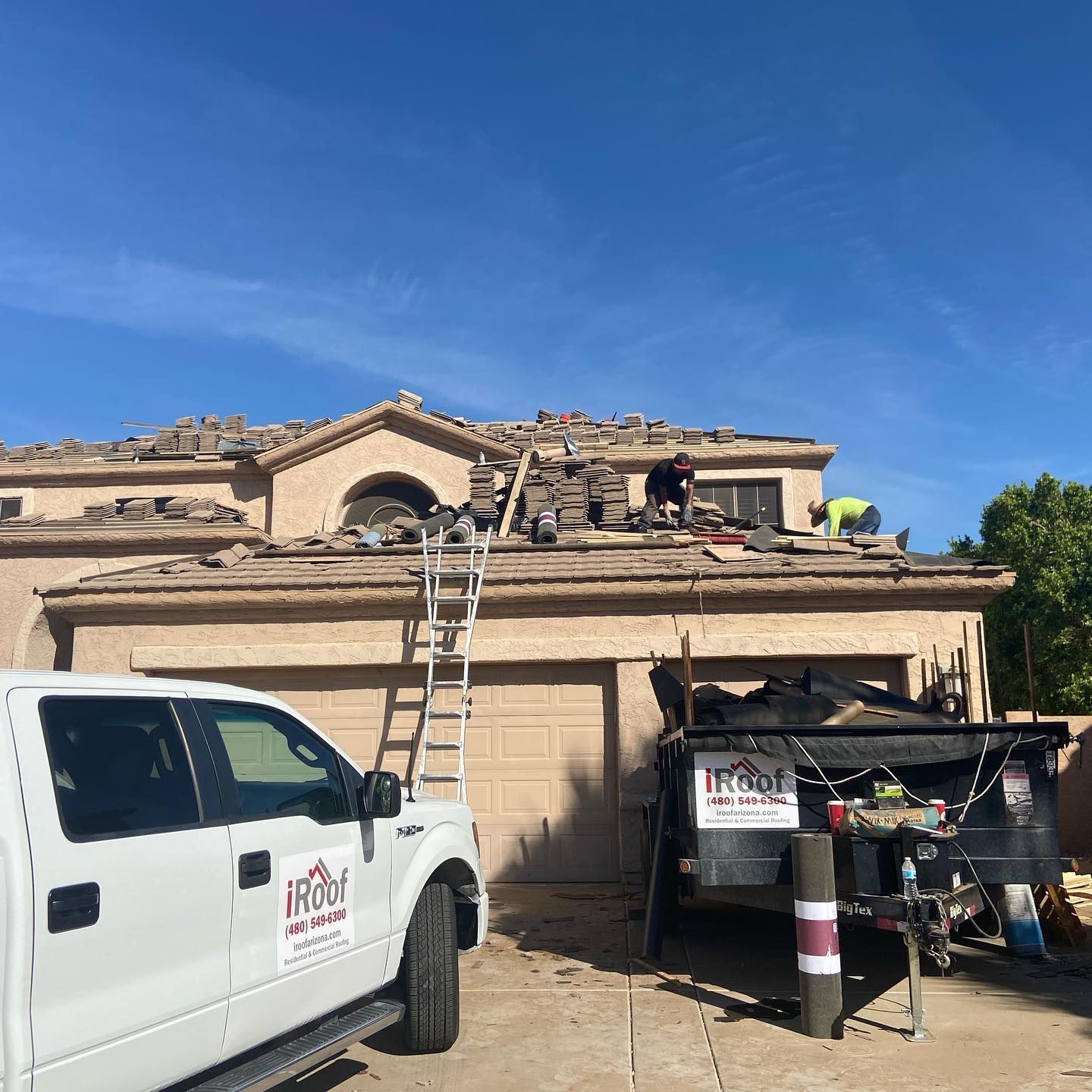 Roofers working on a residential roof, with a truck and trailer in the driveway. Sunny day.