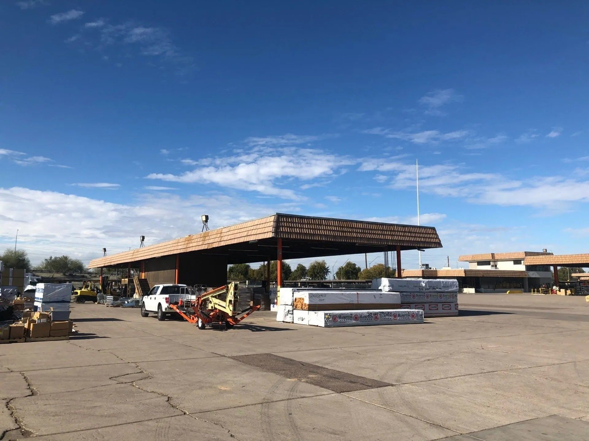 Lumberyard with covered loading area and stacks of wood under a blue sky.