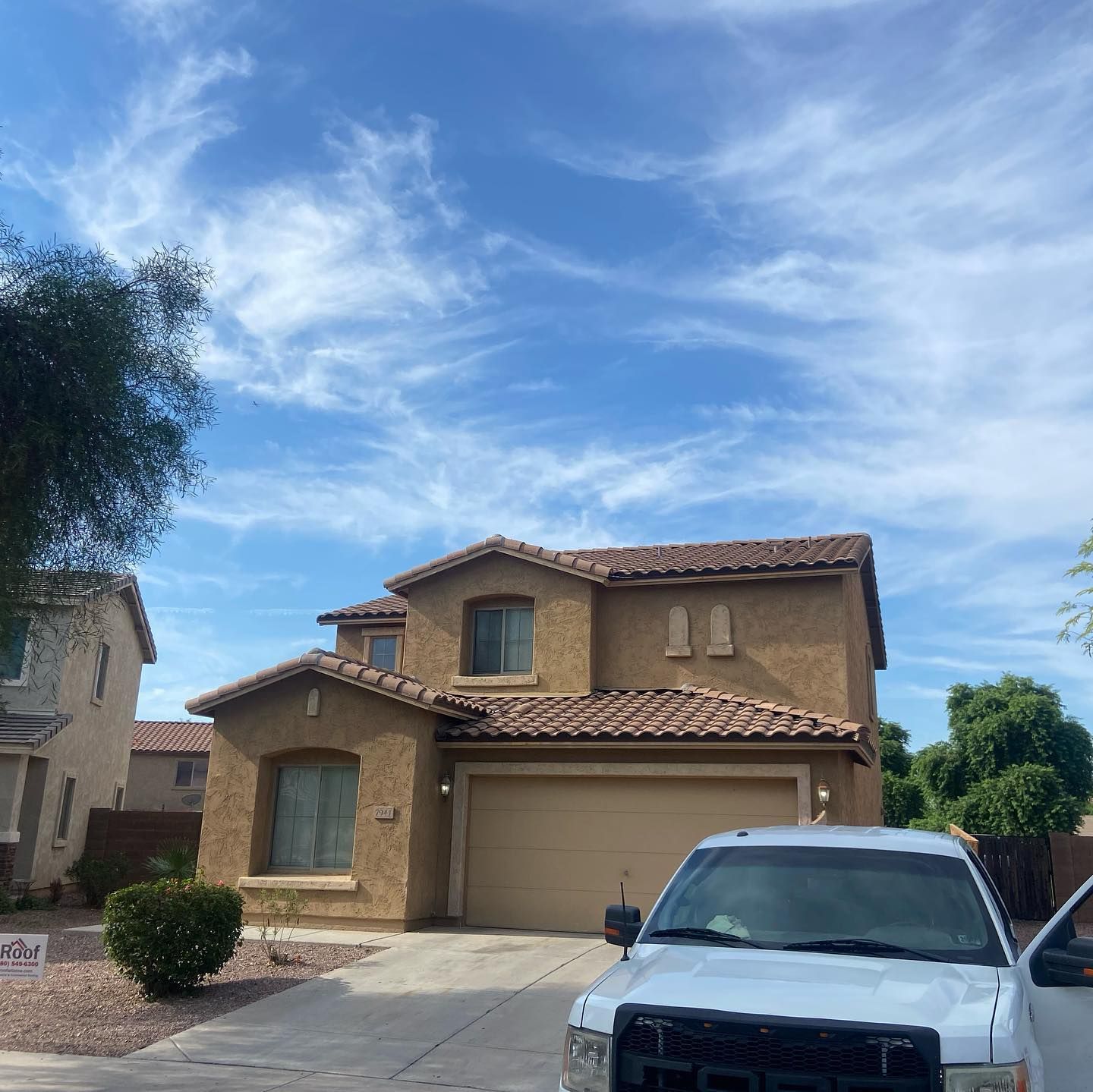 Two-story tan house with a garage, blue sky with whispy clouds, white truck parked in front.