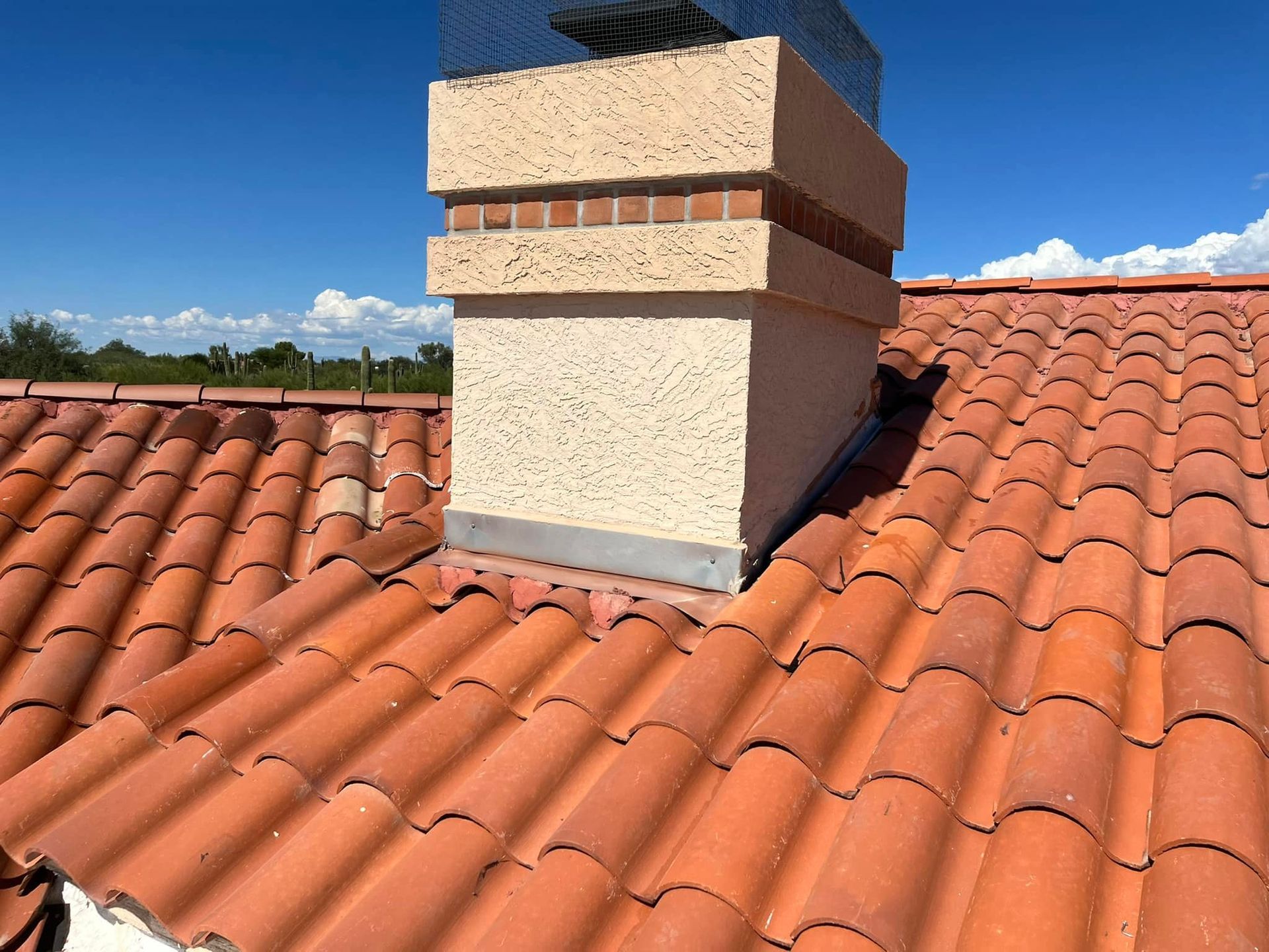Clay tile roof with a textured beige chimney against a blue sky.