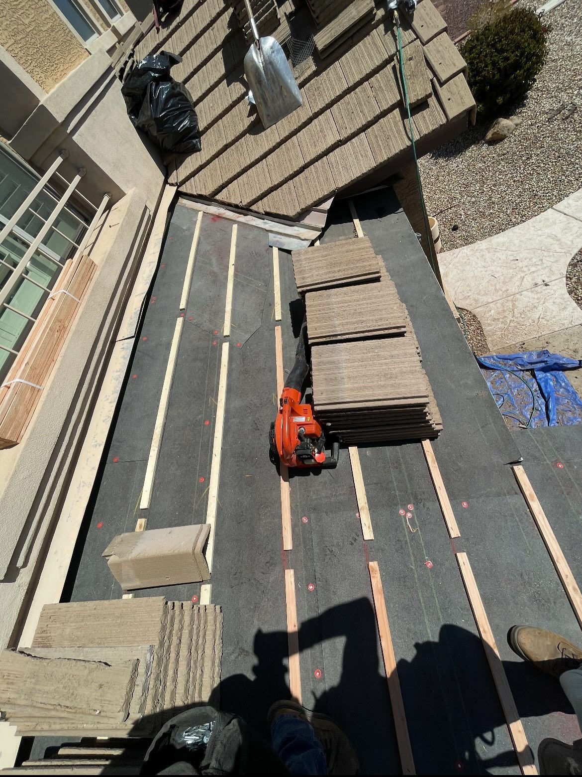 Roofing materials and tools on a flat roof, with stacks of tiles and an orange blower.