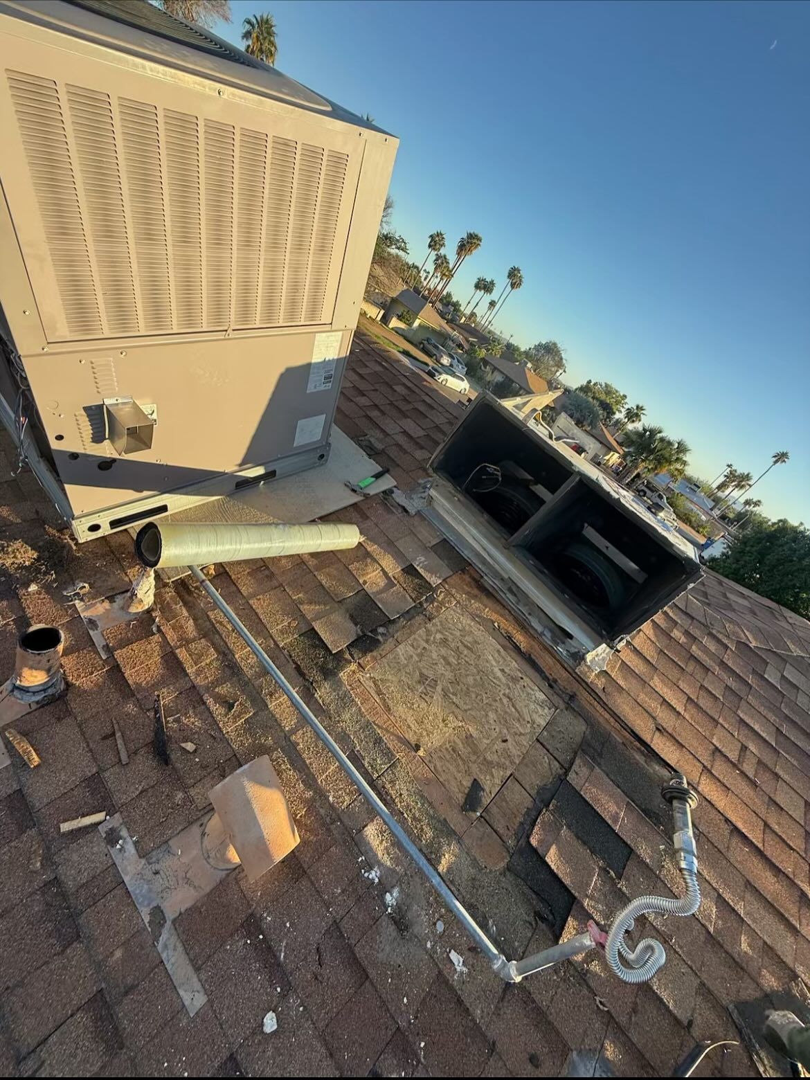 Rooftop with HVAC unit, ductwork, and gas line. Damaged roofing visible. Blue sky in background.