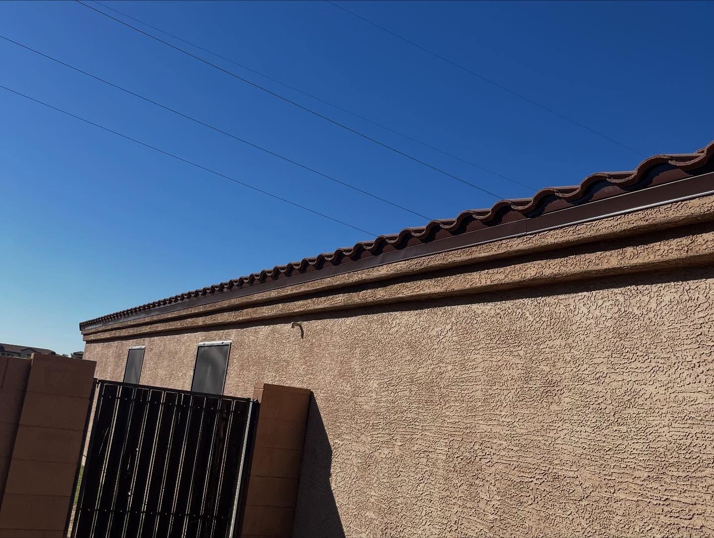Tan stucco wall with brown roof tiles against a clear blue sky.